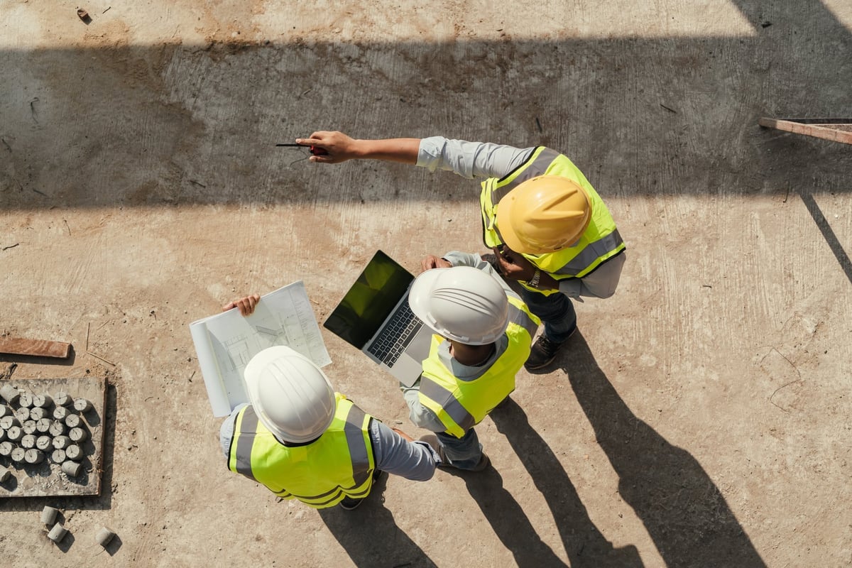 Engineering team inspecting an active construction site with tablet and blueprints