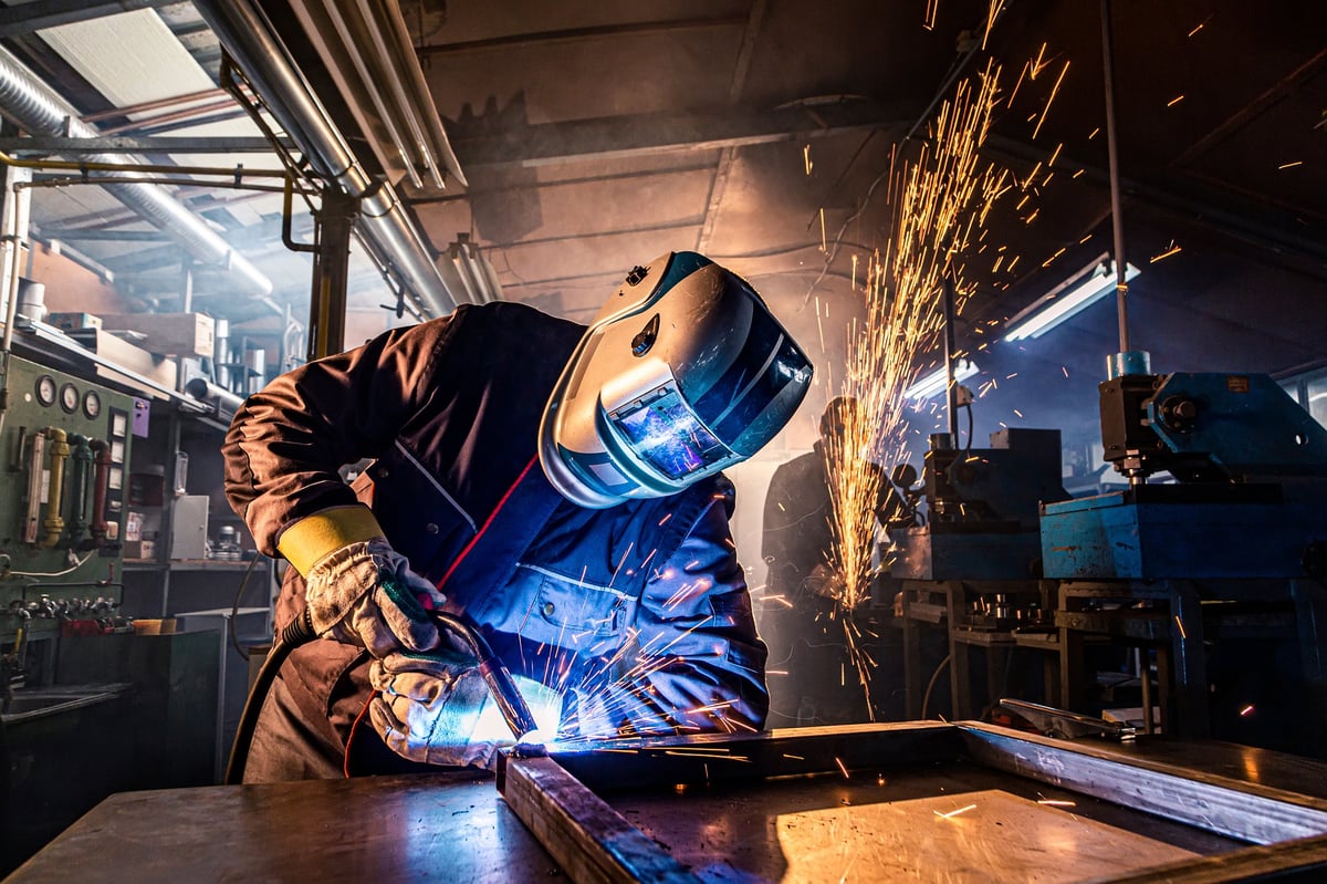 Welder joining metal parts with sparks flying in an active fabrication shop
