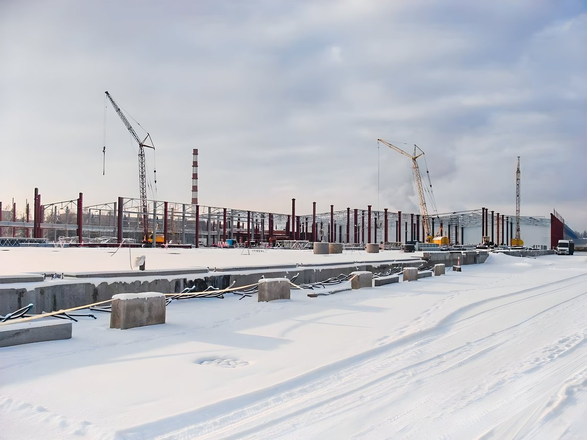 Winter construction site with cranes and a partially built structure in a snowy landscape
