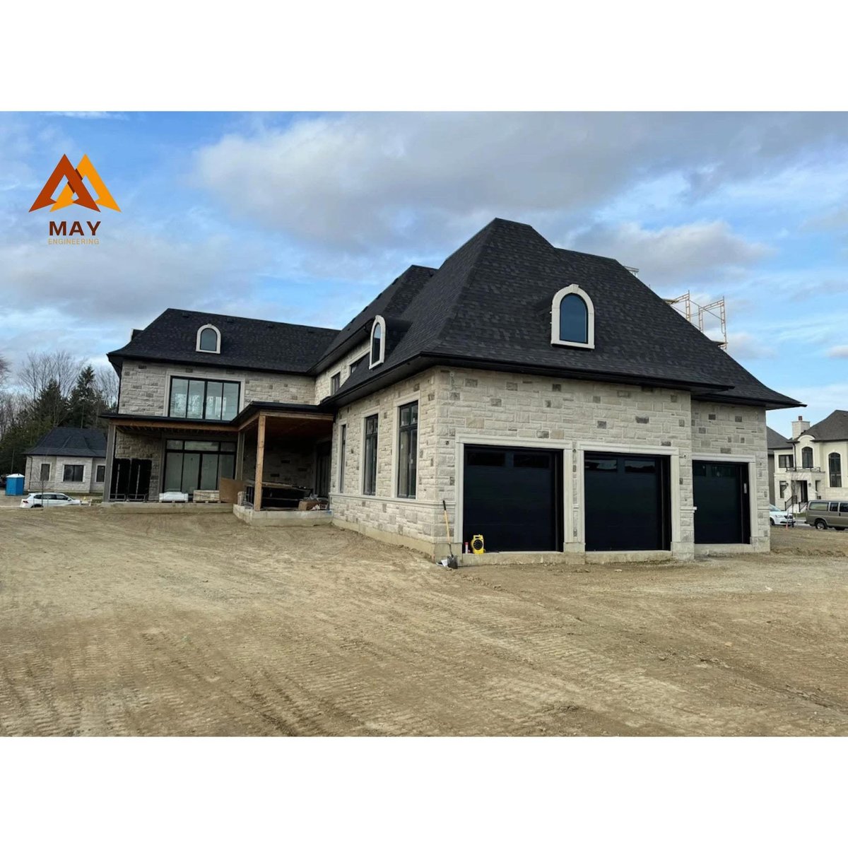 Large two-story stone home under construction with black roof and three-car garage by MAY Engineering — design-build project in Oakville Ontario — MAY Engineering Inc.