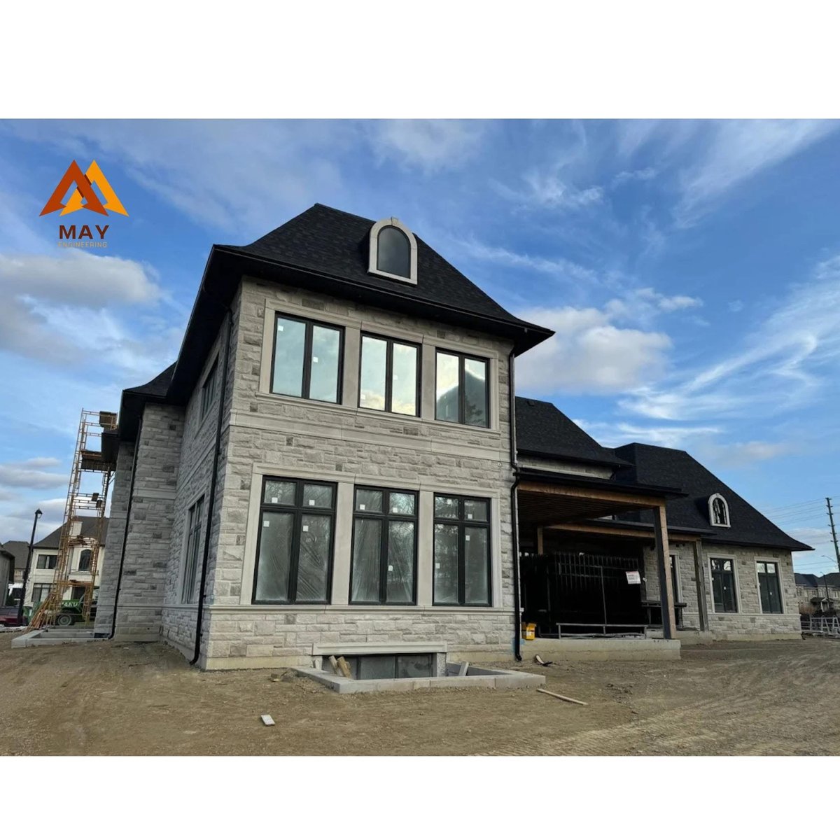 Modern two-story stone house with black roof and garage under construction on empty lot — design-build project in London Ontario — MAY Engineering Inc.