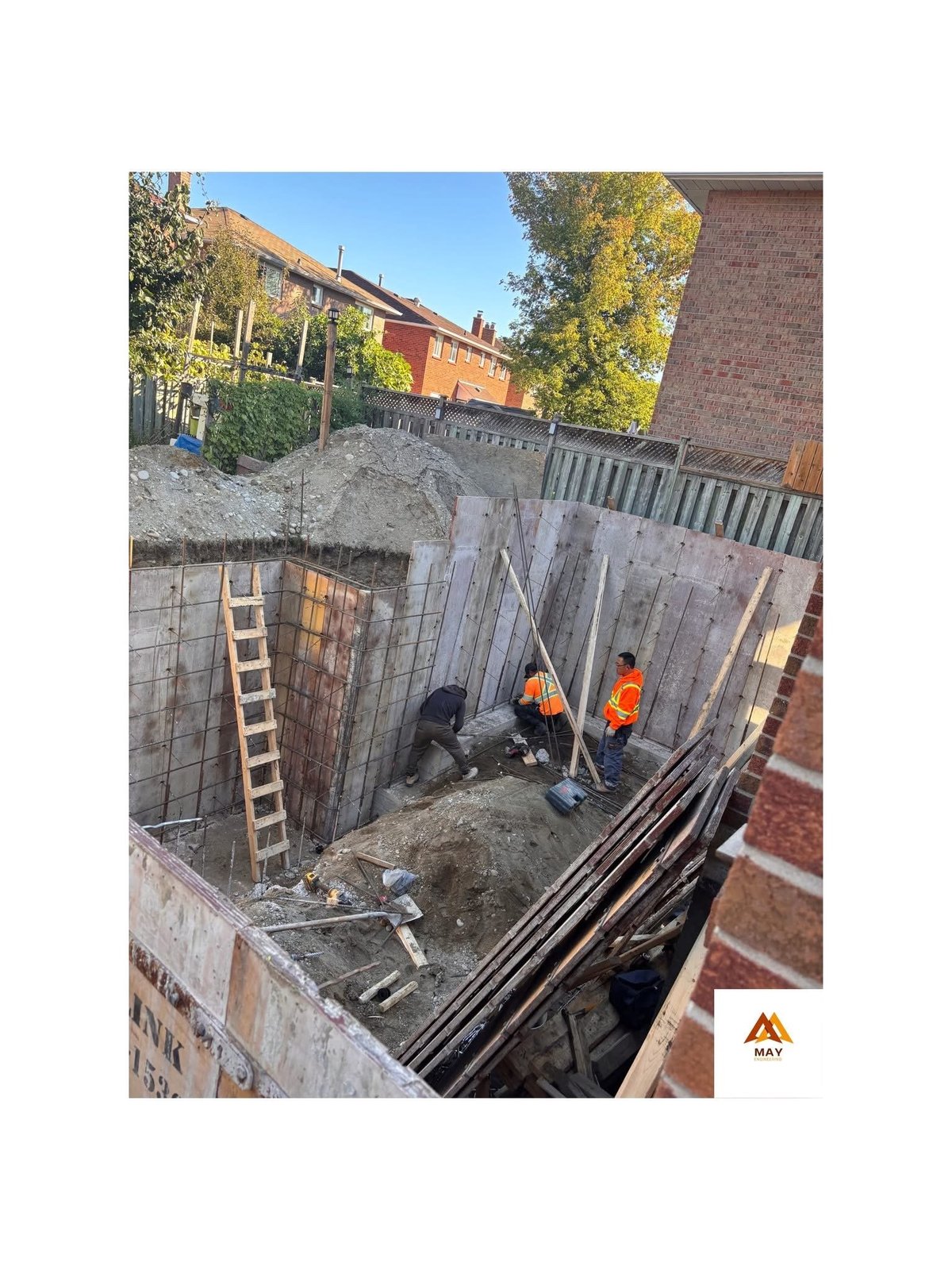 Construction site showing workers in safety vests excavating a deep foundation pit surrounded by metal shoring walls — structural engineering project in Etobicoke Ontario — MAY Engineering Inc.
